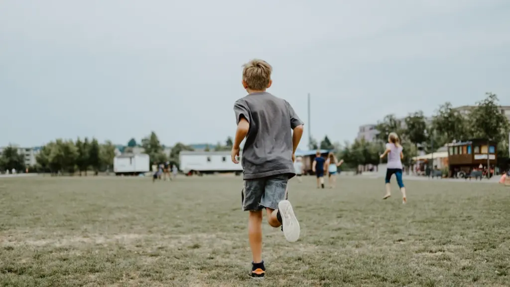 Un jeune garçon court joyeusement sur une grande pelouse verte en extérieur.