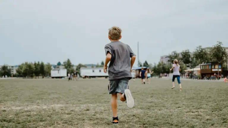 Un jeune garçon court joyeusement sur une grande pelouse verte en extérieur.