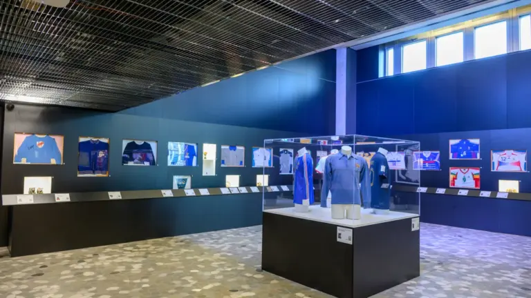 Exposition de maillots de football historiques exposés dans un musée moderne sur fond bleu.