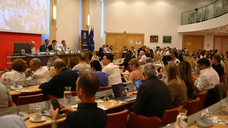 Une assemblée nombreuse assiste à une réunion formelle dans une salle de conférence institutionnelle.