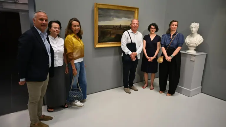 Un groupe de six personnes pose devant un tableau et un buste en musée.