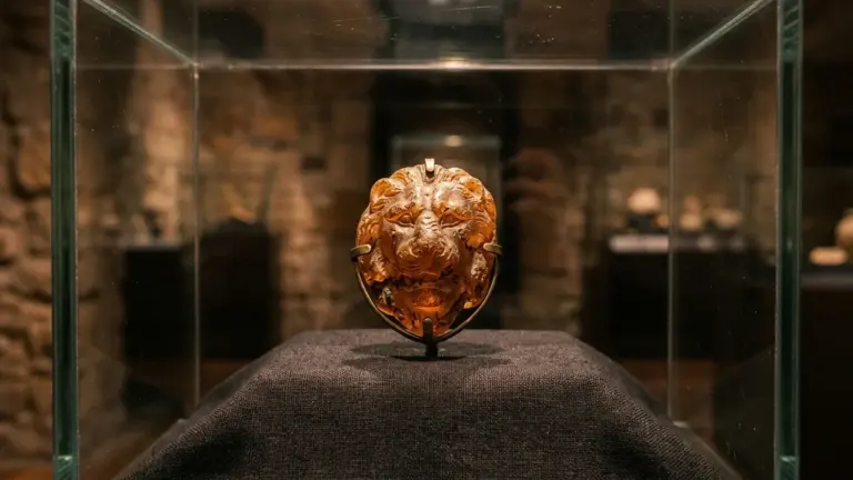 Une tête de lion sculptée en ambre exposée dans une vitrine de musée éclairée.