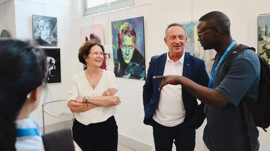 Trois personnes discutent joyeusement dans une galerie d'art contemporain entourées de peintures murales colorées.