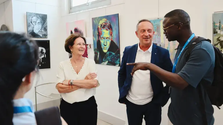 Trois personnes discutent joyeusement dans une galerie d'art contemporain entourées de peintures murales colorées.