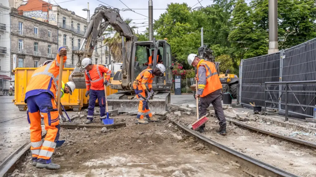 Ouvriers en vêtements de sécurité travaillant sur des voies ferrées avec une pelleteuse en arrière-plan.