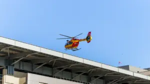 Un hélicoptère médical survole un bâtiment hospitalier sous un ciel bleu dégagé en France.