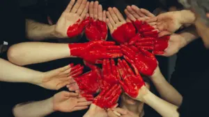 Plusieurs mains peintes en rouge formant un cœur symbolique pour le don du sang.