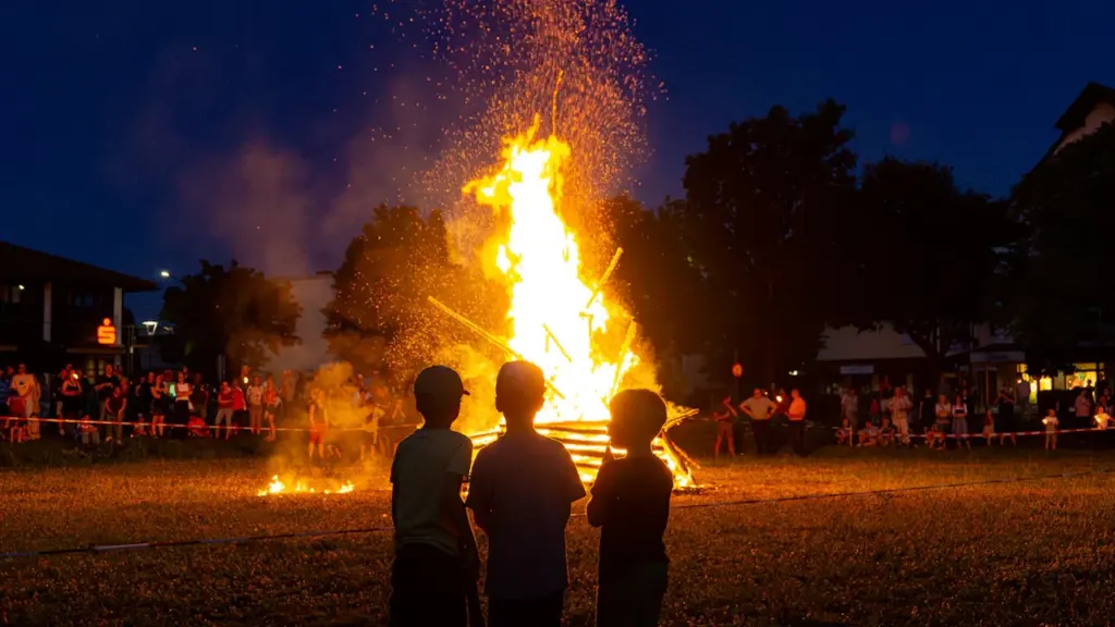 Trois enfants regardent un grand feu de joie nocturne lors d'un événement festif.