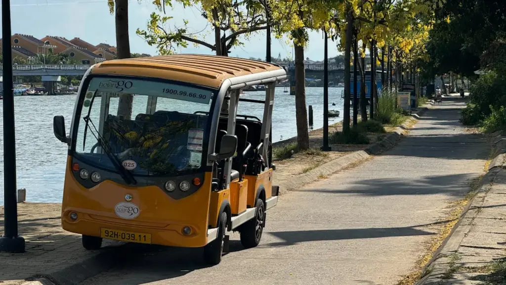 Une navette électrique jaune stationnée au bord d'une rivière en été.