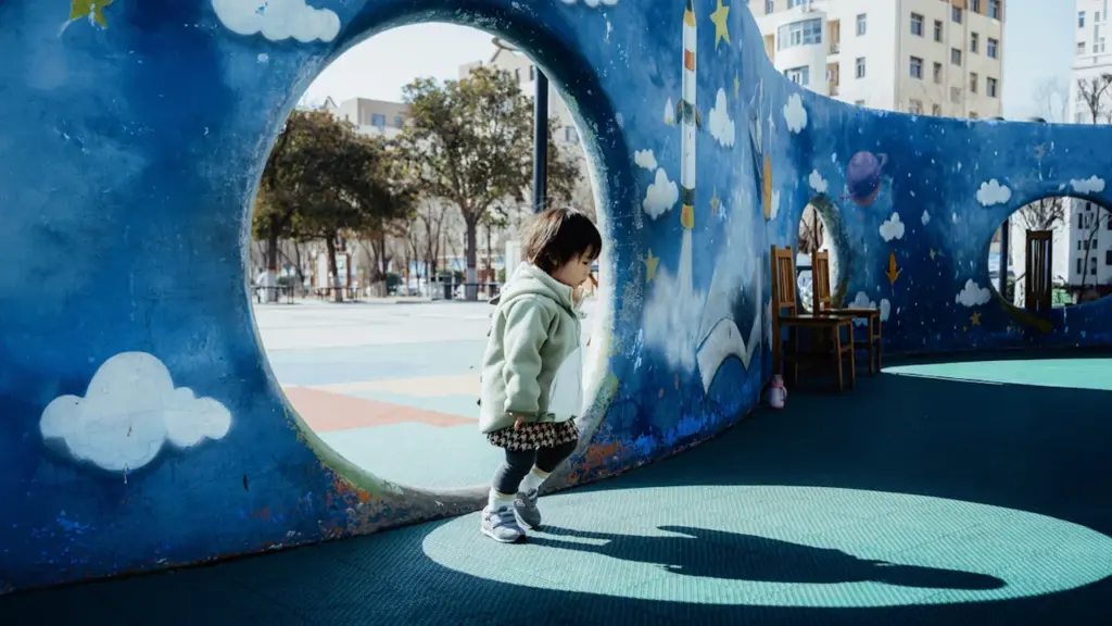 Une enfant marche dans un tunnel de jeu coloré sur une aire de jeux.