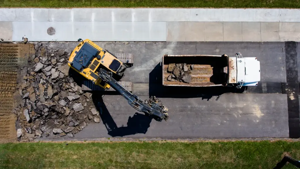 Vue aérienne d'une pelleteuse jaune retirant de l'asphalte sur un chantier urbain.