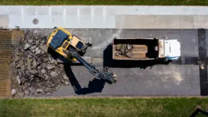 Vue aérienne d'une pelleteuse jaune retirant de l'asphalte sur un chantier urbain.