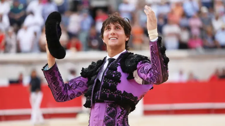 Un jeune torero en costume violet et noir salue la foule dans une arène.