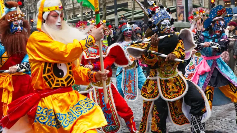 Artistes en costumes traditionnels colorés participant à un défilé festif dans les rues de Paris.