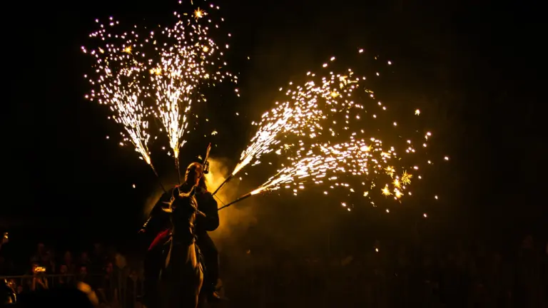 Un cavalier à cheval portant des feux d'artifice scintillants lors d'un spectacle nocturne impressionnant.