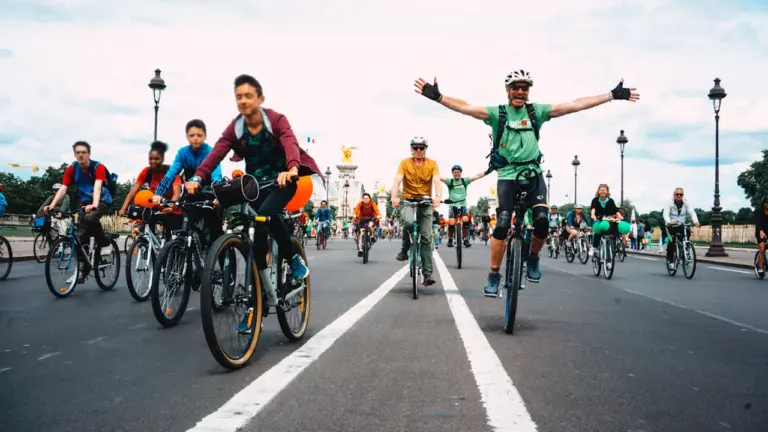 Groupe de cyclistes joyeux pédalant sur une large avenue parisienne ensoleillée.