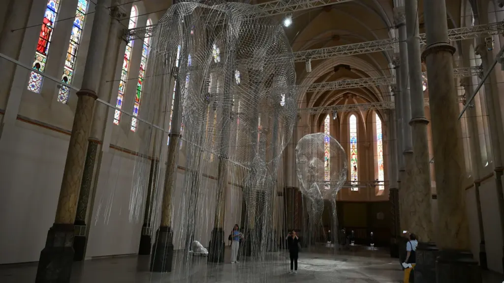 Deux sculptures en grillage métallique suspendues à l'intérieur d'une église avec des vitraux.