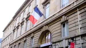Bâtiment institutionnel français en pierre arborant fièrement le drapeau tricolore à l'entrée.
