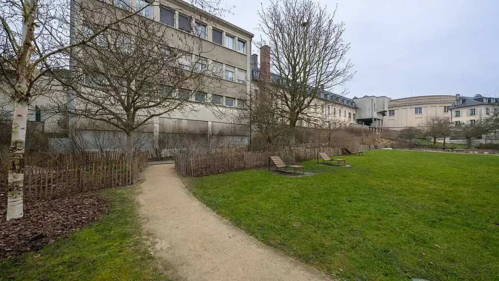 Un sentier sablonneux traverse une pelouse avec des chaises longues près de grands bâtiments anciens.
