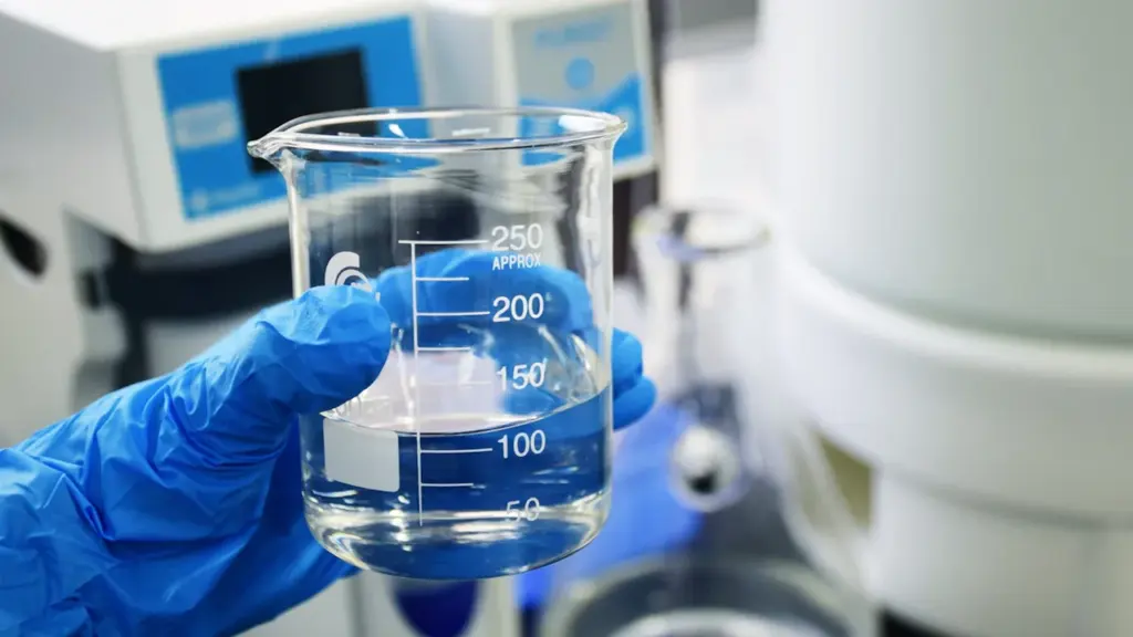 Une main gantée tenant un bécher rempli d'eau dans un environnement de laboratoire.