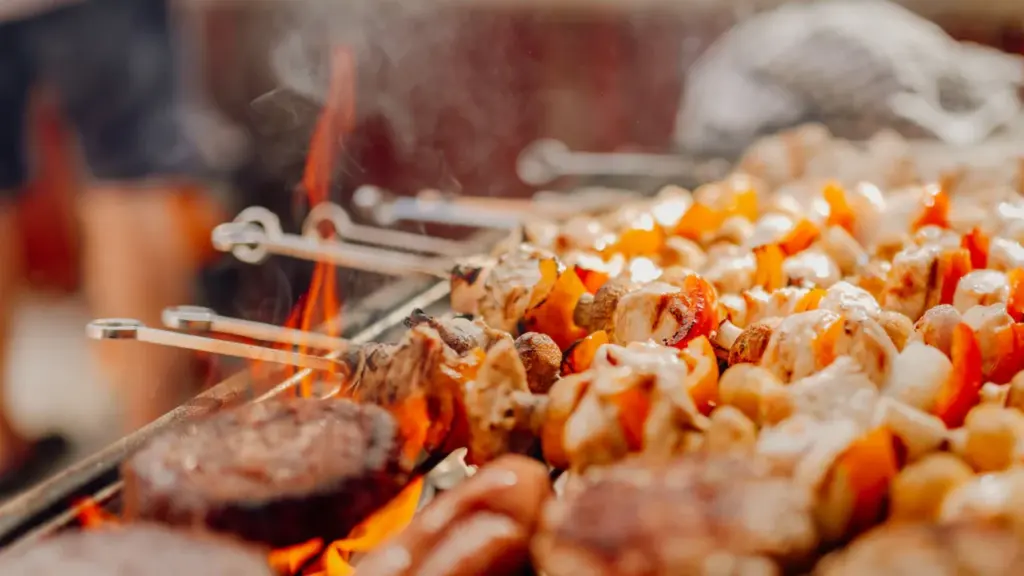 Brochettes et viandes grillées sur un barbecue en extérieur lors d'une journée ensoleillée.