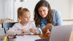 Une mère souriante montre quelque chose sur un ordinateur portable à sa jeune fille attentive.