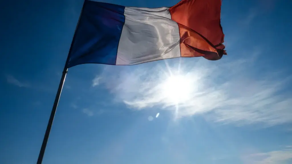 Un drapeau français flottant sous un soleil éclatant dans un ciel bleu dégagé.