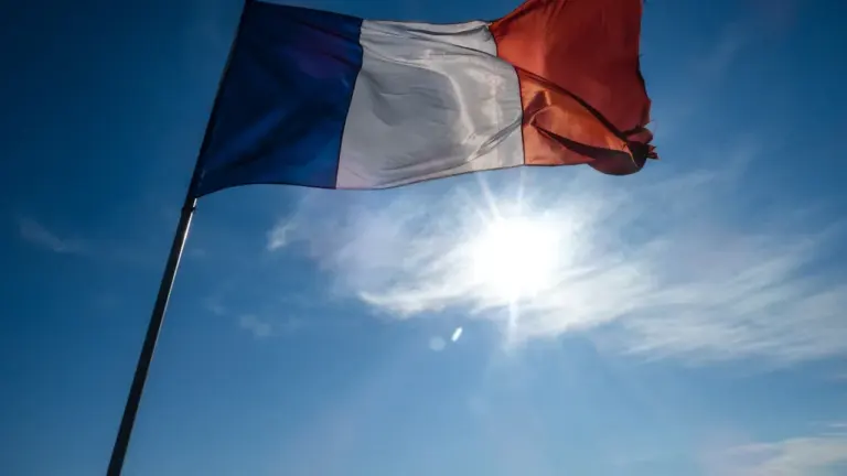 Un drapeau français flottant sous un soleil éclatant dans un ciel bleu dégagé.