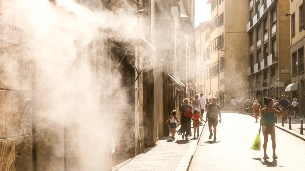 Passants marchant dans une rue ensoleillée sous une brume rafraîchissante pendant la canicule.