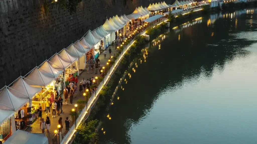 Vue aérienne d'un marché nocturne le long d'une rivière avec des stands alignés.