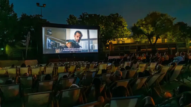 Un public regarde un film en plein air sur un écran géant la nuit.