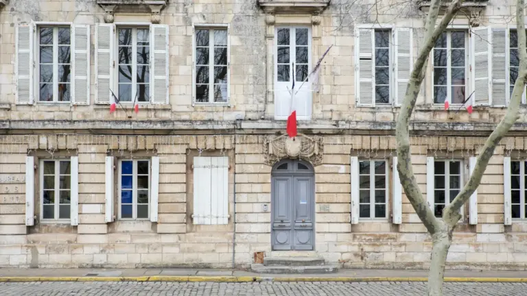 Façade traditionnelle d'une mairie française avec ses fenêtres typiques et drapeau tricolore.