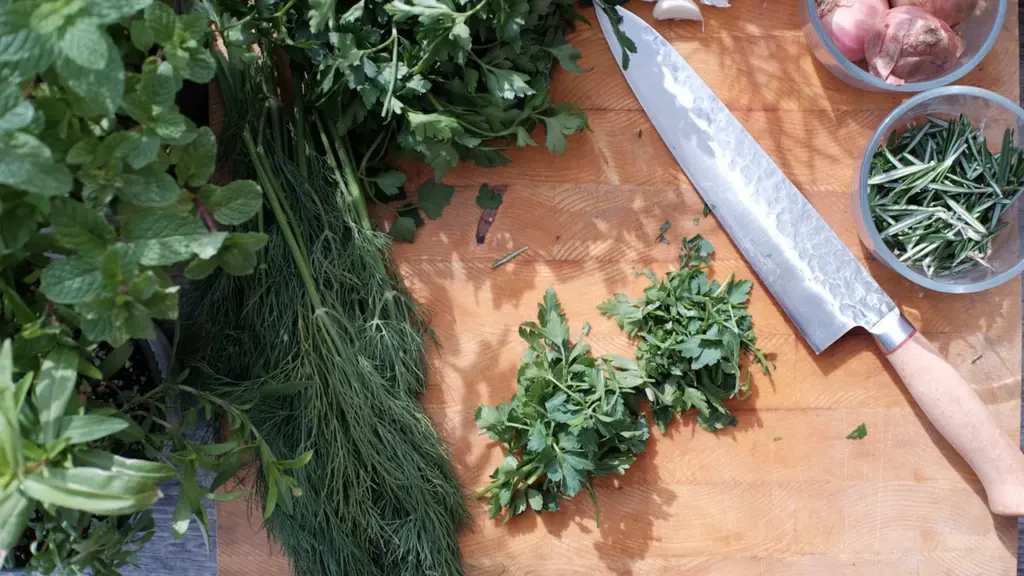 Planche à découper en bois avec des herbes aromatiques fraîches et un couteau.