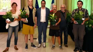 Un groupe de six personnes souriantes tenant des plantes en pot lors d'une cérémonie officielle.