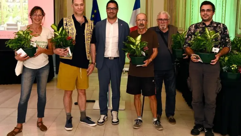 Un groupe de six personnes souriantes tenant des plantes en pot lors d'une cérémonie officielle.