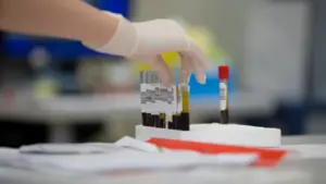 Une main gantée manipulant des tubes de prélèvement sanguin dans un laboratoire médical.