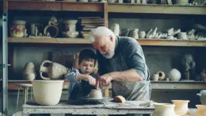 Un grand-père transmet son savoir-faire artisanal à son petit-fils lors d'un atelier poterie.