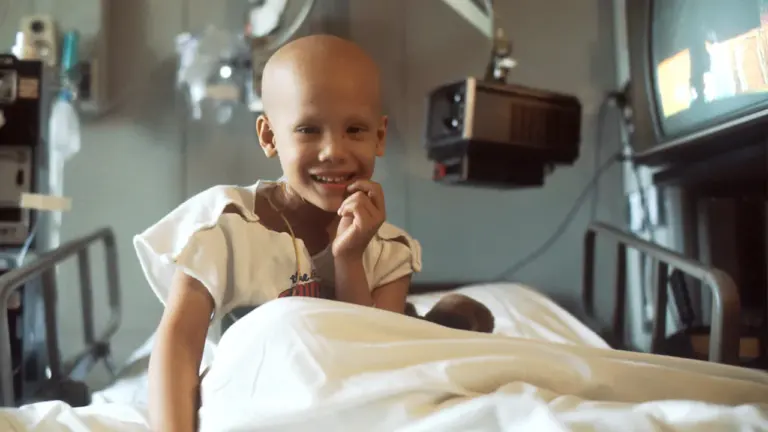Une jeune enfant souriante assise sur son lit d'hôpital, illustrant le soutien aux soins pédiatriques.